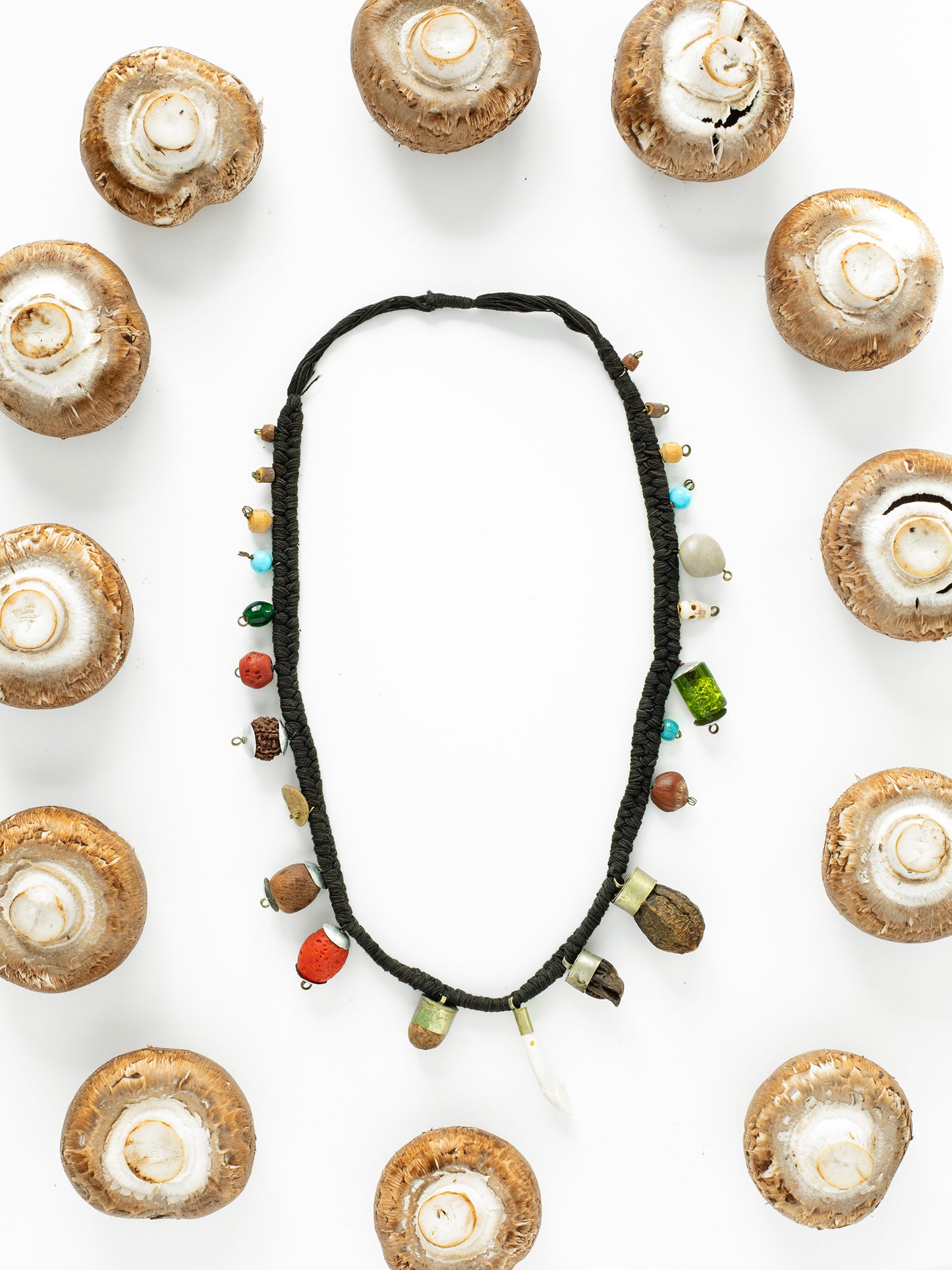 A vintage Tibetan shaman mala charm necklace displayed against a white background, surrounded by mushrooms.