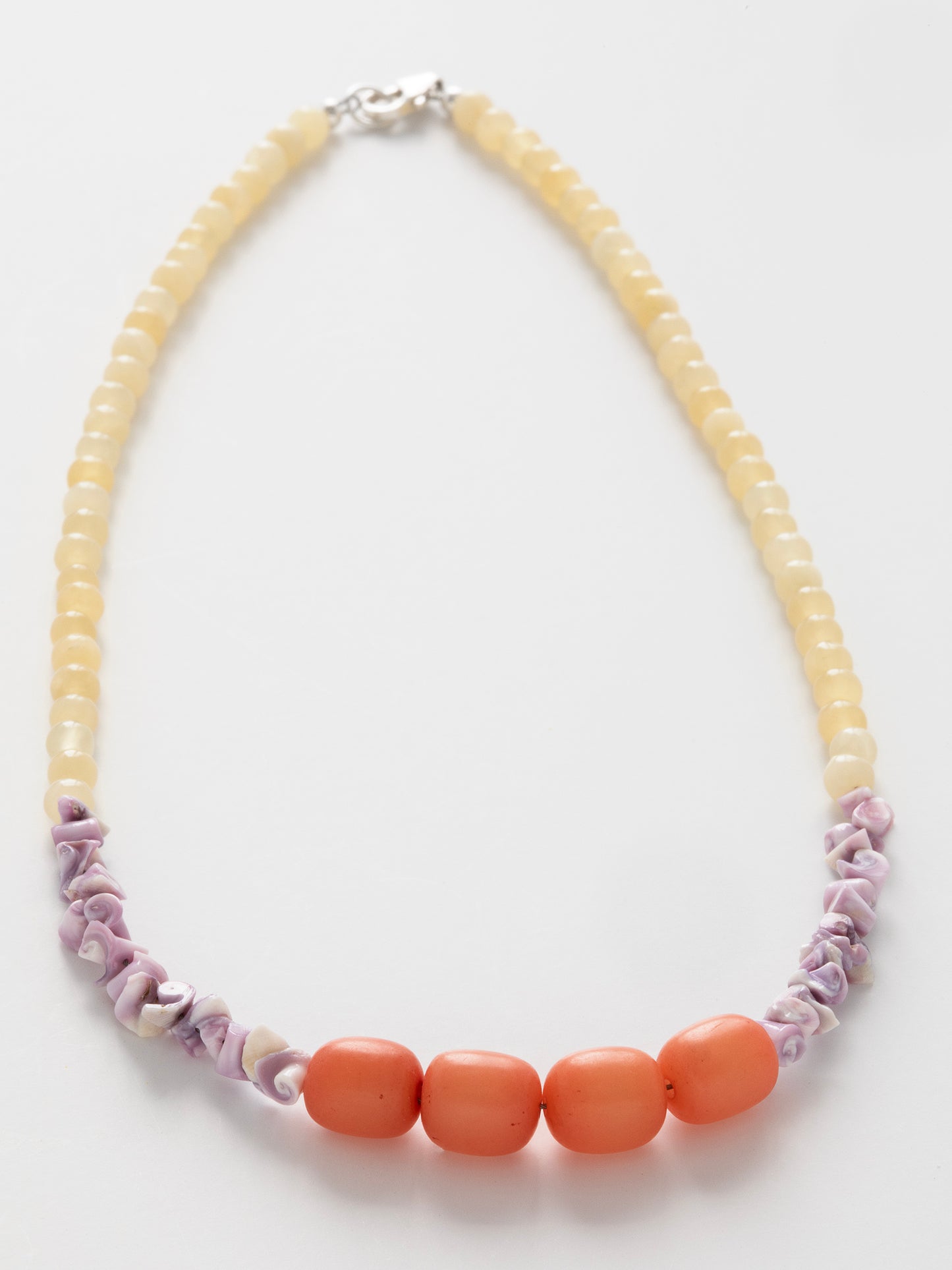 Close-up photo of a delicate hand-beaded necklace with light yellow Citrine, purple Sea Urchin shell beads, & peach-colored Buri Seed beads.