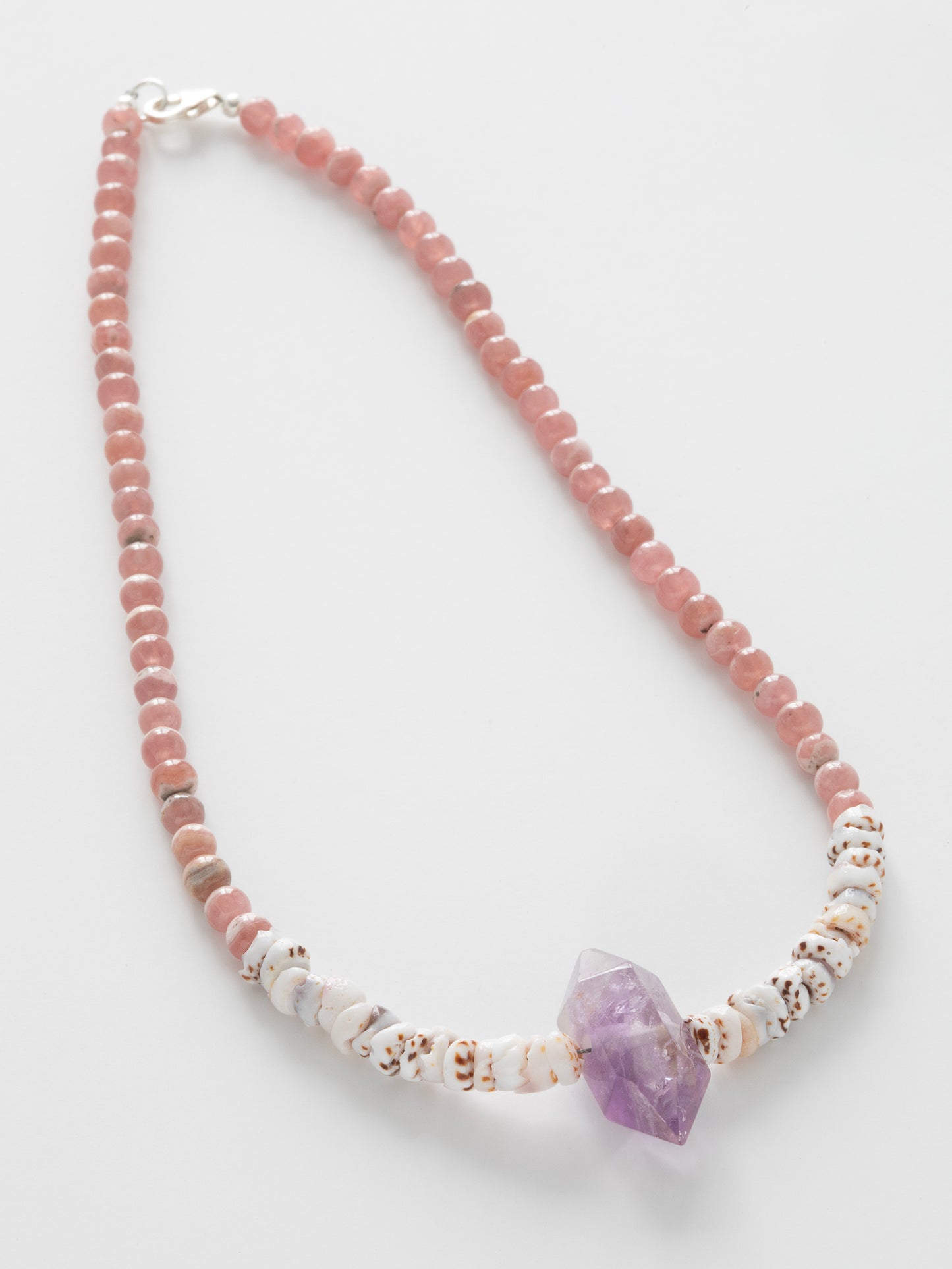 A necklace with a combination of pink Rhodochrosite, purple Amethyst stones, & natural Puka Shells, featuring a Sterling Silver clasp.
